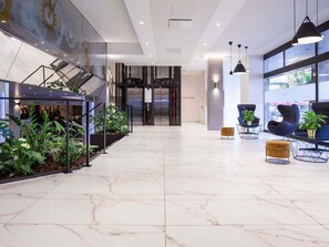A modern lobby with a marble floor, seating area with chairs and tables, a staircase with glass railings, and a large window with a view. - Mercure Plaza Biel (Biel)
