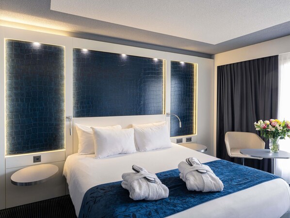 A modern hotel room with a large bed, a bedside table, a chair, and a small table with a vase of flowers. - Mercure Plaza Biel (Biel)