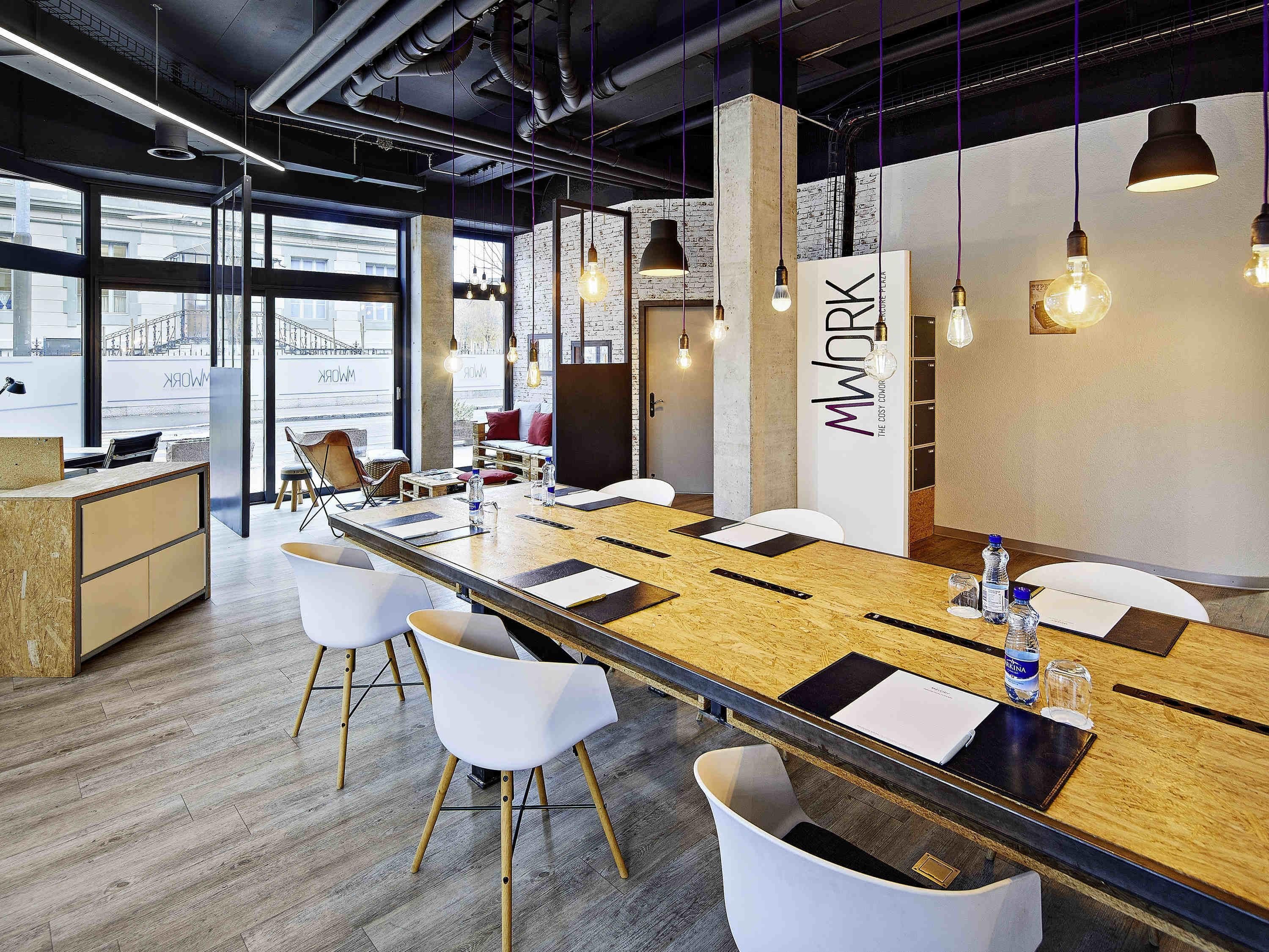A modern conference room with a long table, white chairs, and hanging pendant lights.