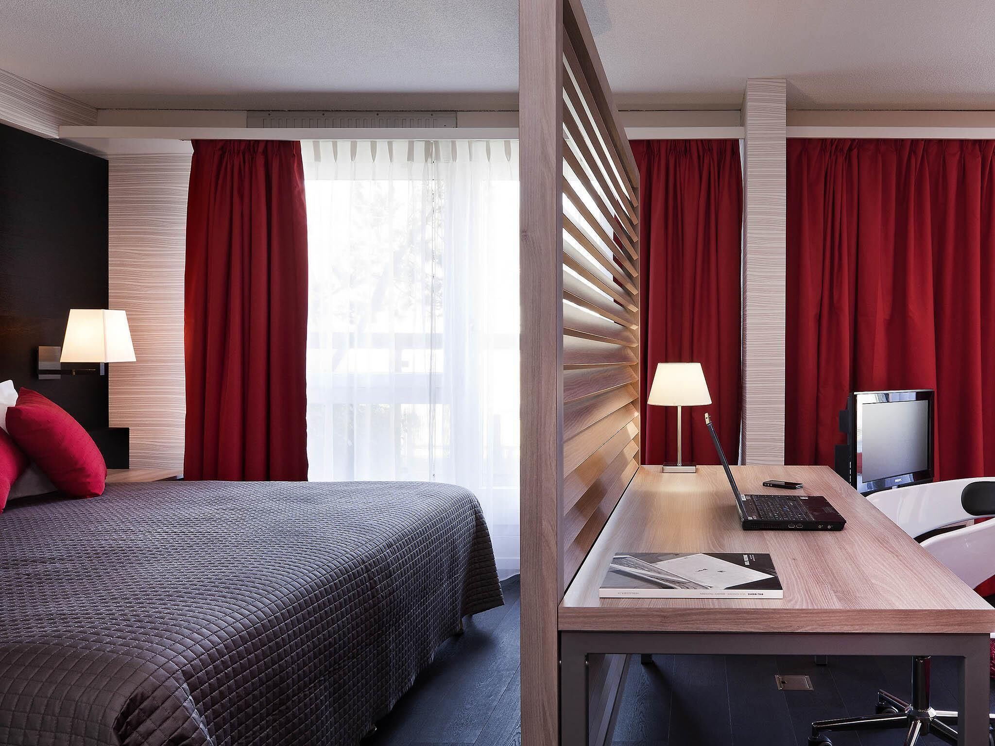 Ein Hotelzimmer mit einem Bett, einem Schreibtisch mit Computer und einem Fernseher.