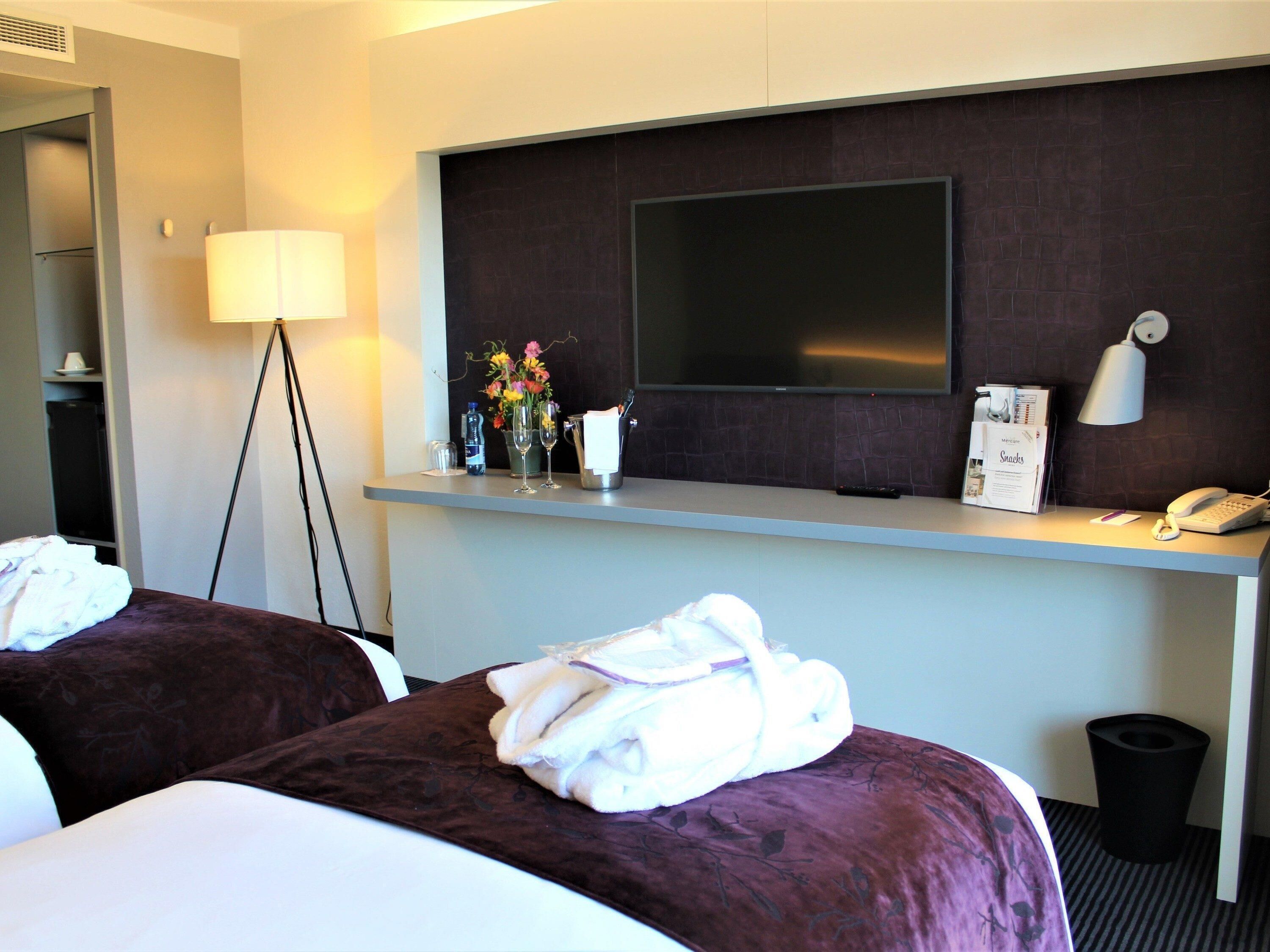 Une chambre d’hôtel avec deux lits, un bureau doté d’un téléviseur à écran plat, une lampe et une poubelle.