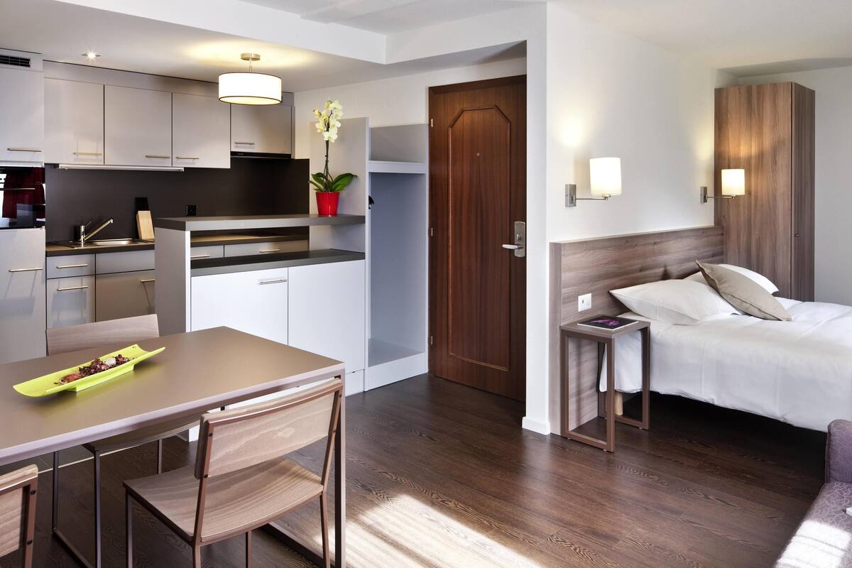 A modern hotel room with a wooden floor, a bed with white linens, a small bedside table, and a nightstand.