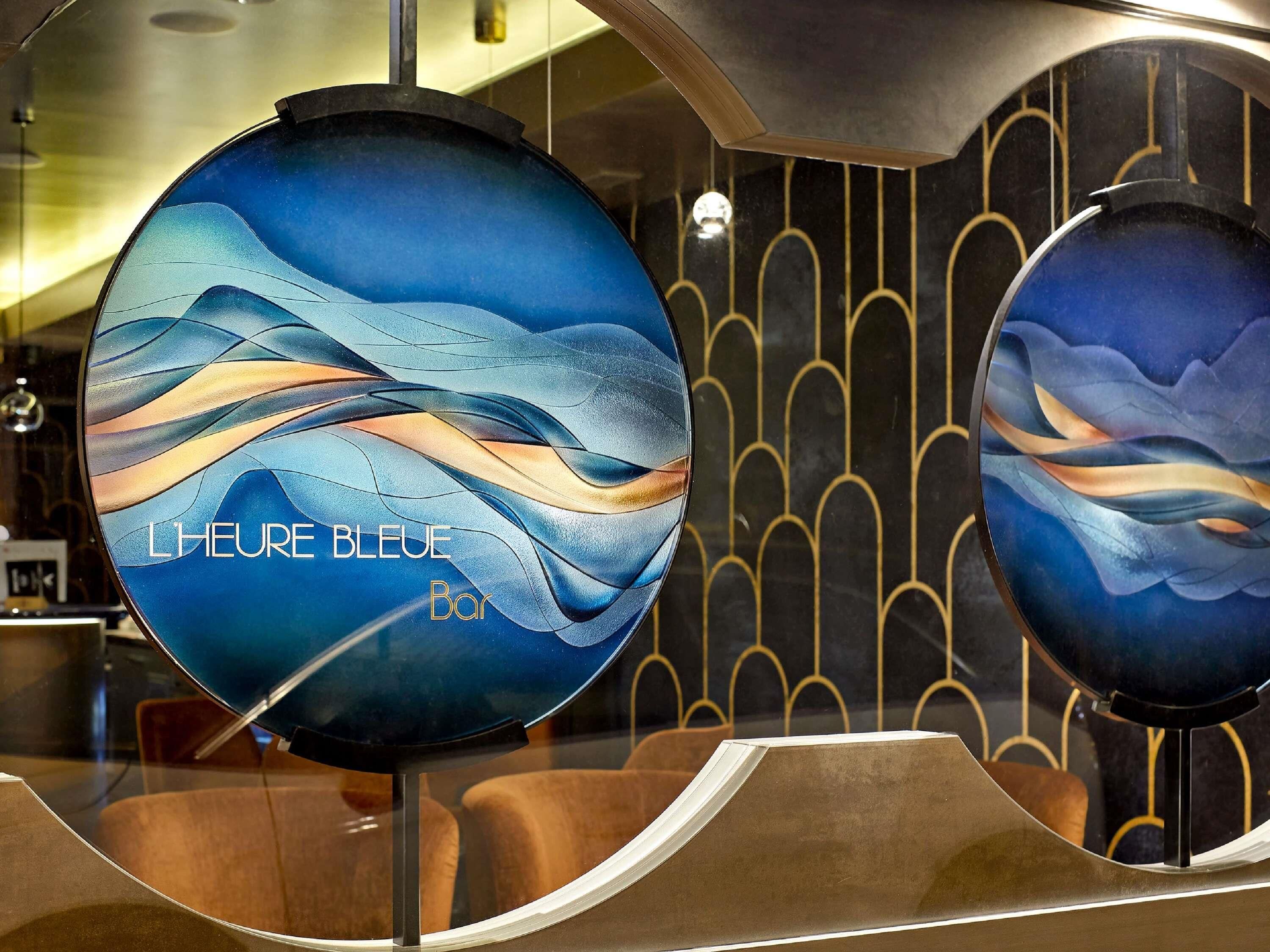 A circular, modern-designed mirror with a blue abstract pattern and the text 'L'HEURE BLEUE Bar'.