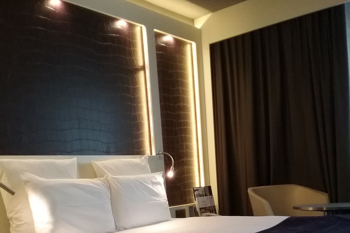 A hotel room with a large bed, a chair, a desk, and a window with curtains.
