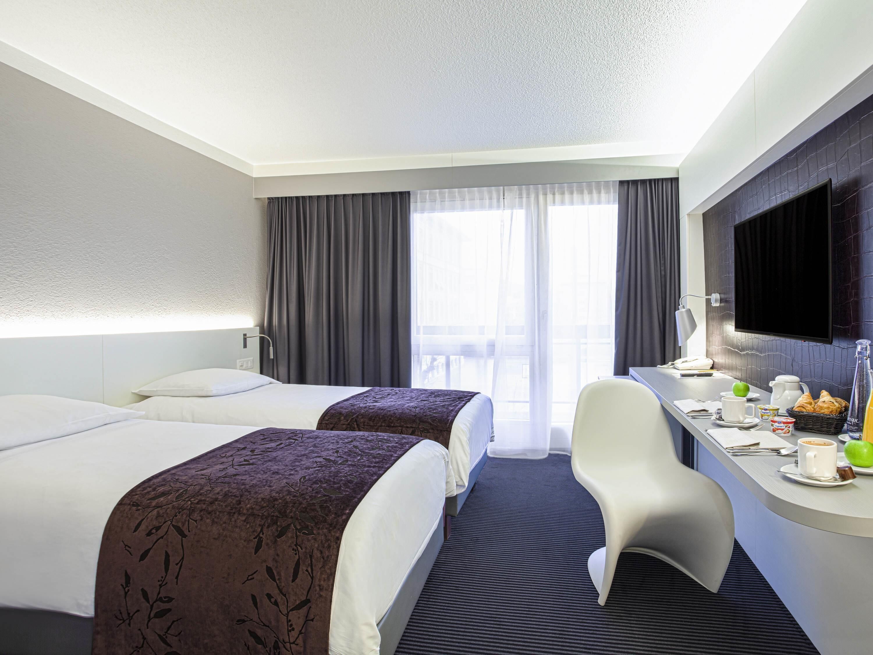 Habitación de hotel con dos camas, un escritorio con alimentos para el desayuno, televisión y vistas al balcón.