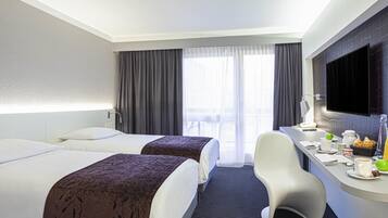 Habitación de hotel con dos camas, un escritorio con alimentos para el desayuno, televisión y vistas al balcón.