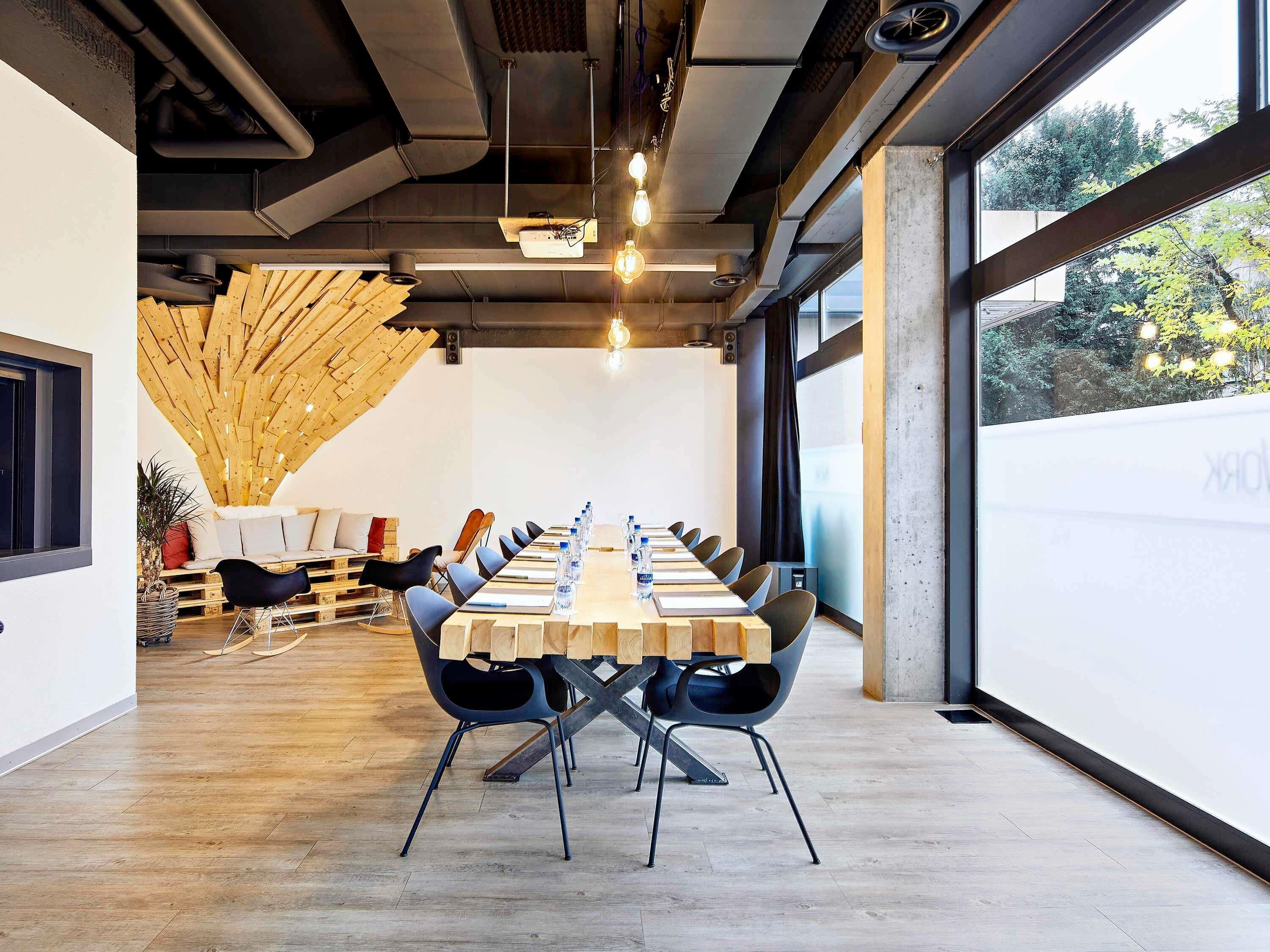 Une salle de conférence dotée d’une longue table, de chaises noires et d’une structure de plafond en bois.