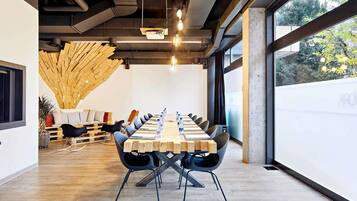 Une salle de conférence dotée d’une longue table, de chaises noires et d’une structure de plafond en bois.
