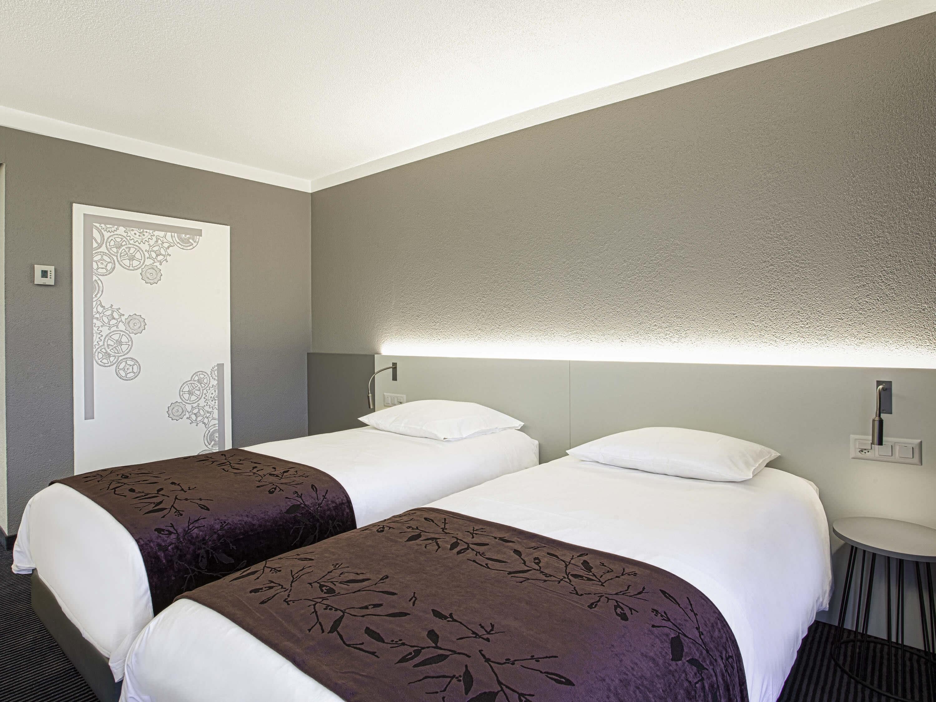Une chambre d’hôtel avec deux lits, une petite table ronde et un luminaire fixé au mur.