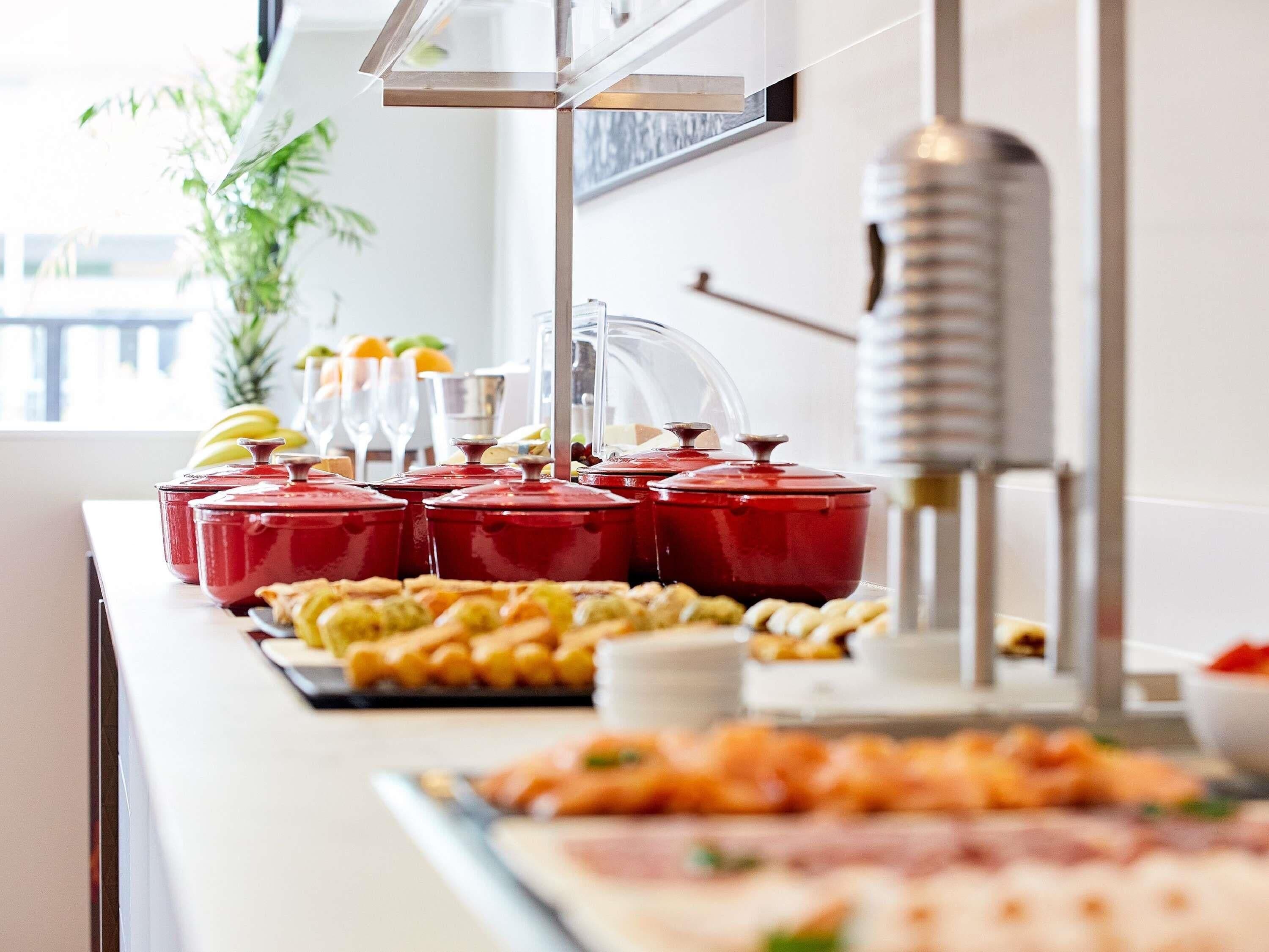 A buffet setup with various food items and red pots on a counter.