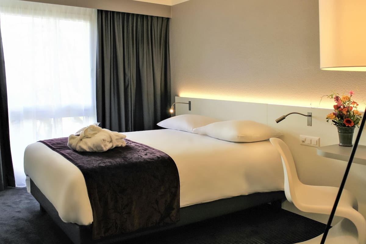 A hotel room with a bed, a chair, a lamp, and a vase with flowers.