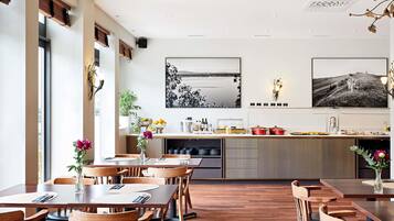 Ein moderner Essbereich mit Holztischen und -stühlen, eine Küche mit Ausblick und Kunstwerken an den Wänden.