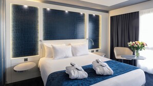 Une chambre d’hôtel moderne avec un grand lit, deux tables de chevet, une petite table ronde et une chaise. Un vase rempli de fleurs est posé sur la table.