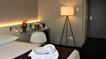 Une chambre d’hôtel avec un lit, un bureau doté d’une lampe, une chaise et un peignoir posé sur le lit.