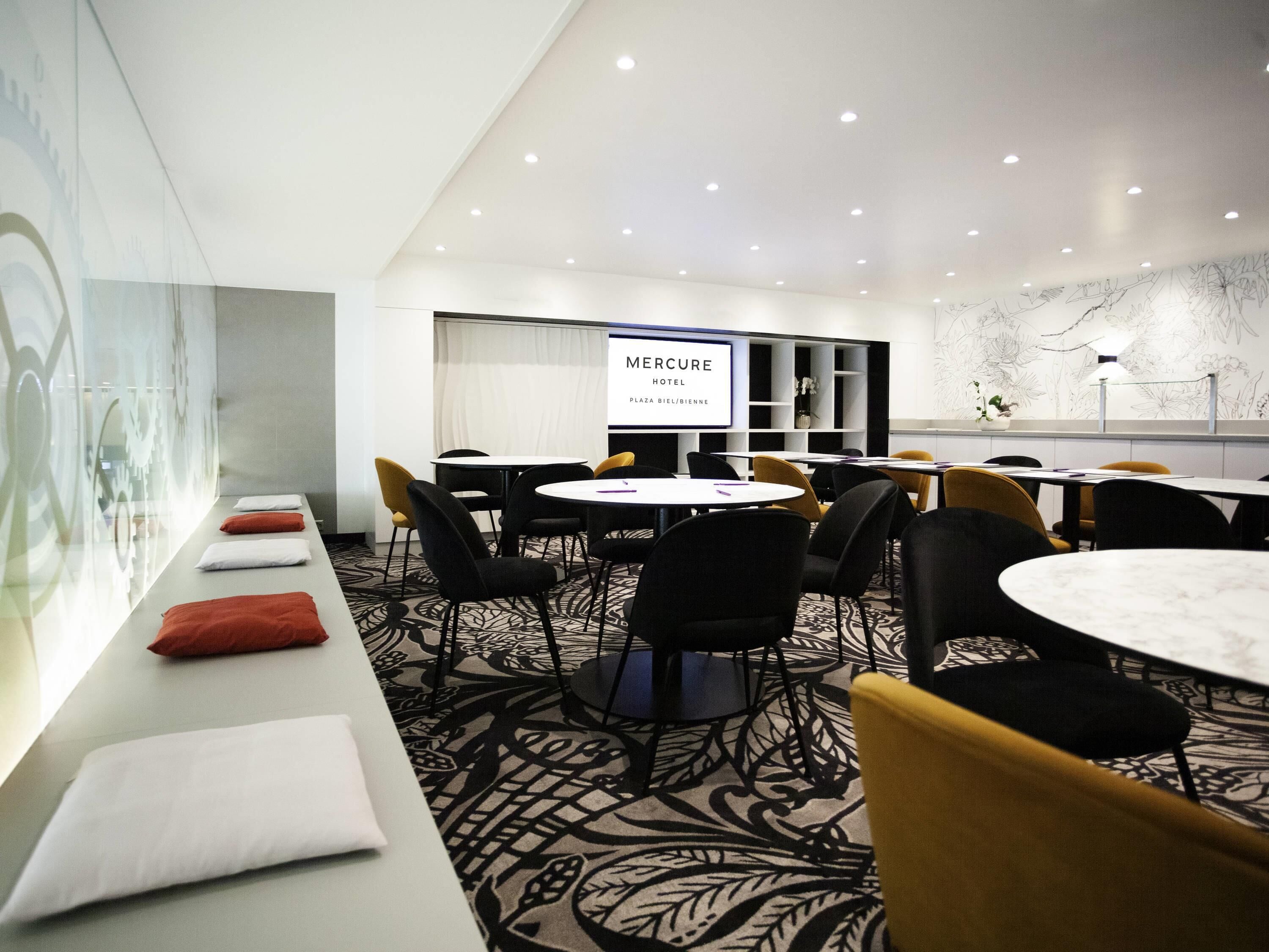 A conference room with a long table, chairs, a projector screen, and a wall with a floral pattern.
