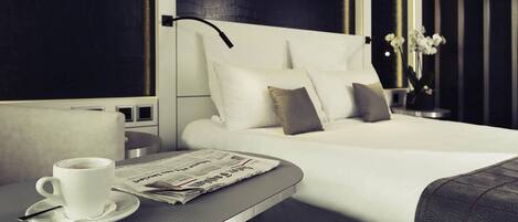 A modern hotel room with a neatly made bed, a bedside table with a cup and newspaper, and a vase with flowers.