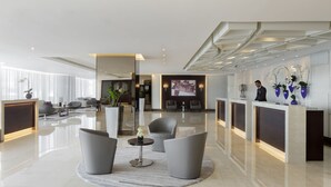A modern hotel lobby with a reception desk, seating area, and decorative plants.