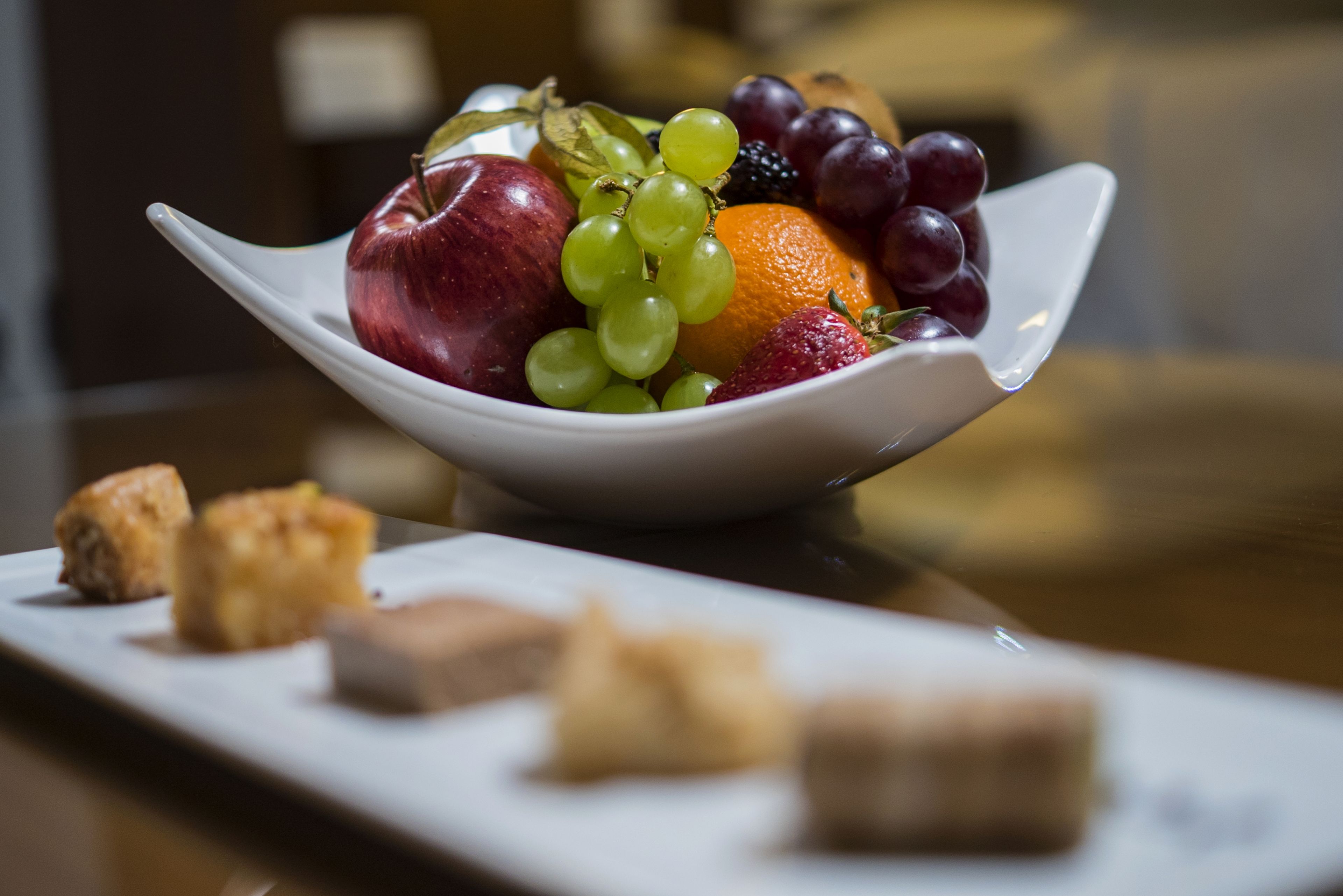 A white bowl filled with fruits and pastries on a white plate.
