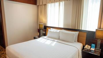 A hotel room with a bed, a nightstand with a lamp, a telephone, and a window with curtains.