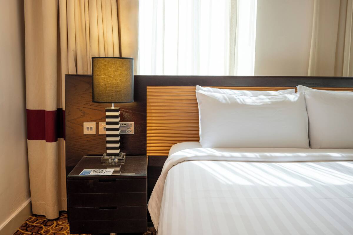 Une chambre d’hôtel avec un lit, une table de chevet, une lampe, une prise de courant et des rideaux.