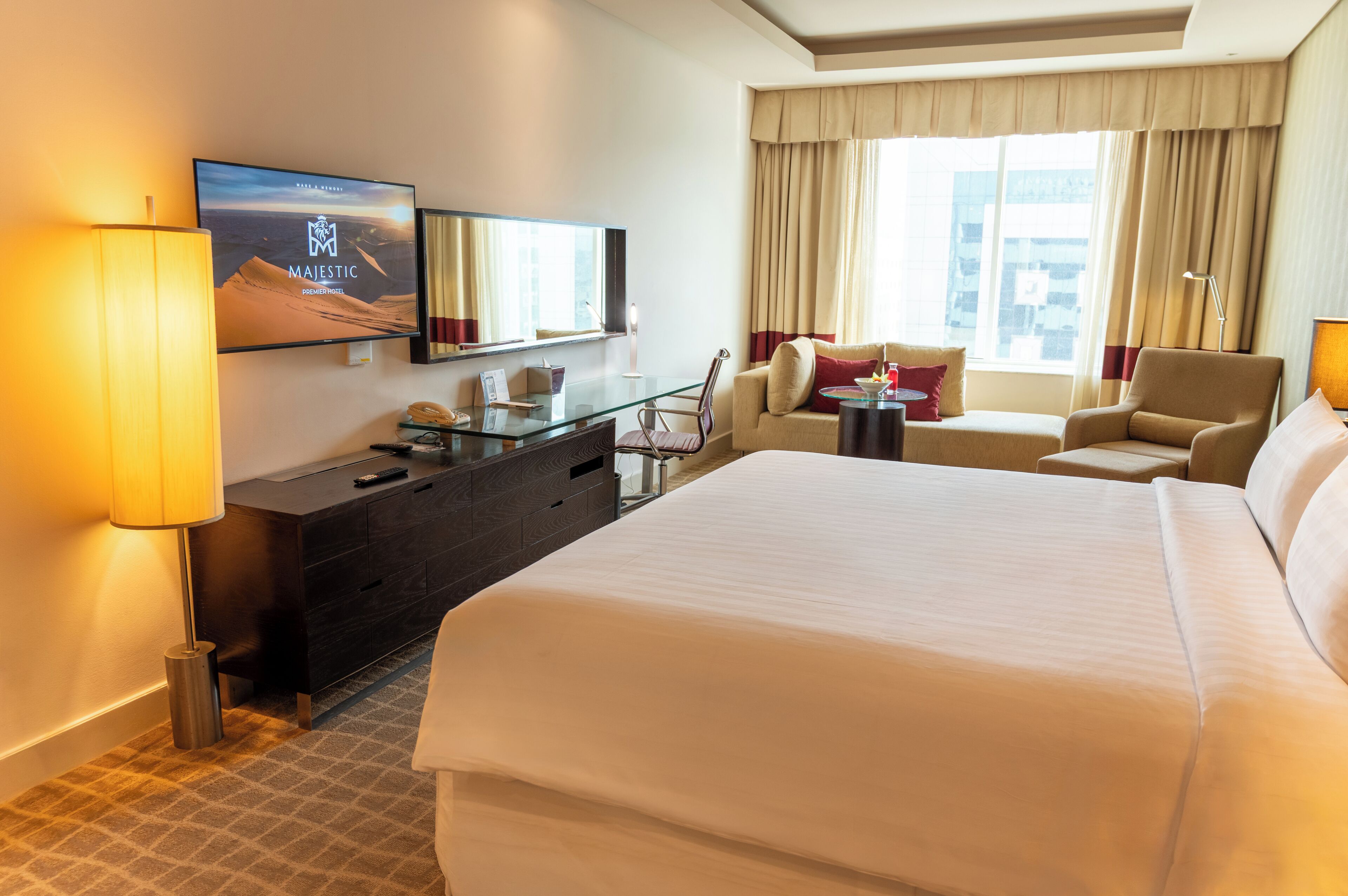 Una camera d'albergo con un letto grande, una scrivania con la televisione, una sedia, un divano e una finestra con tende.