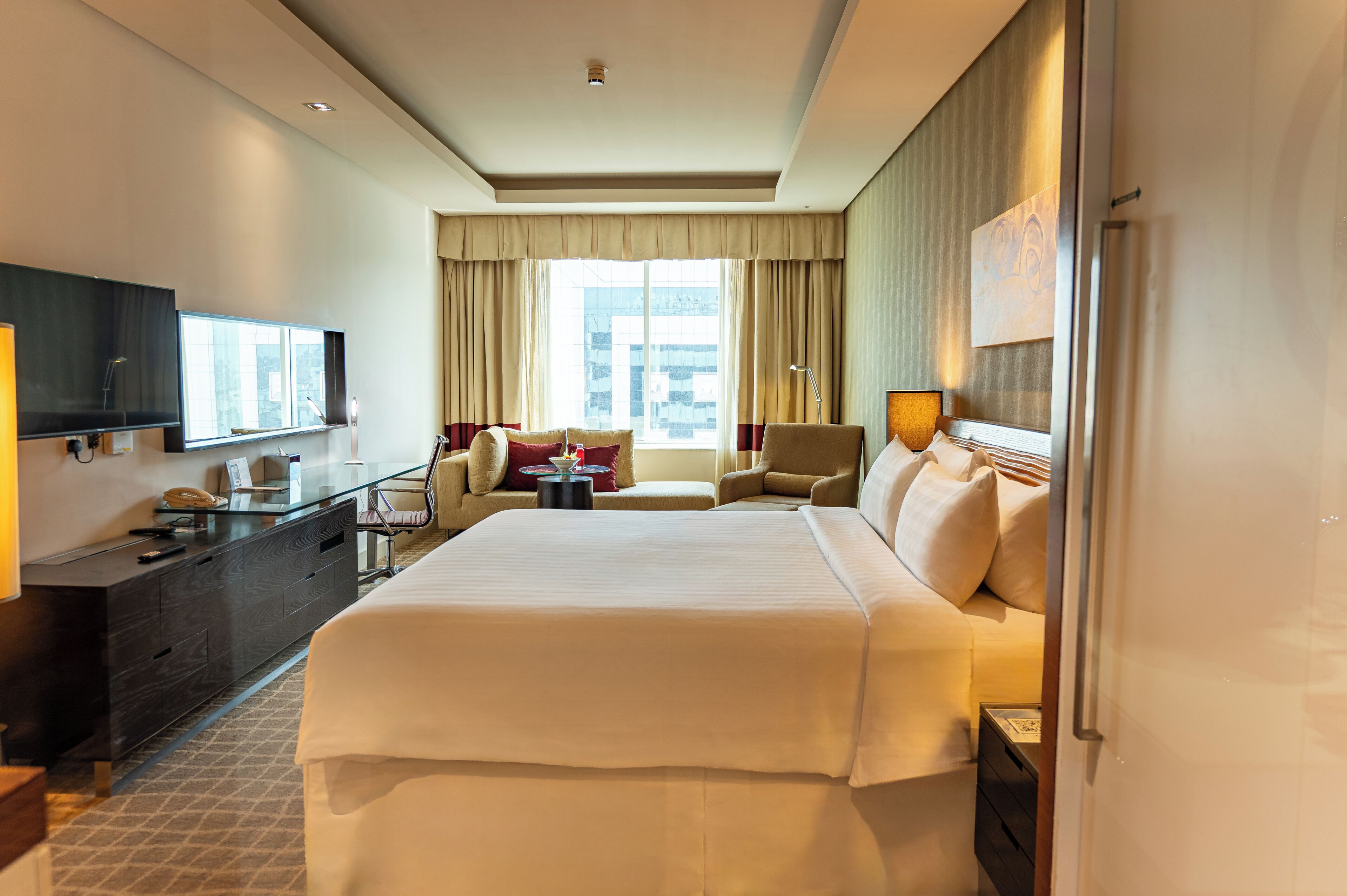 Une chambre d’hôtel avec un grand lit, un bureau doté d’un téléviseur à écran plat, une chaise, un canapé et une fenêtre avec des rideaux.