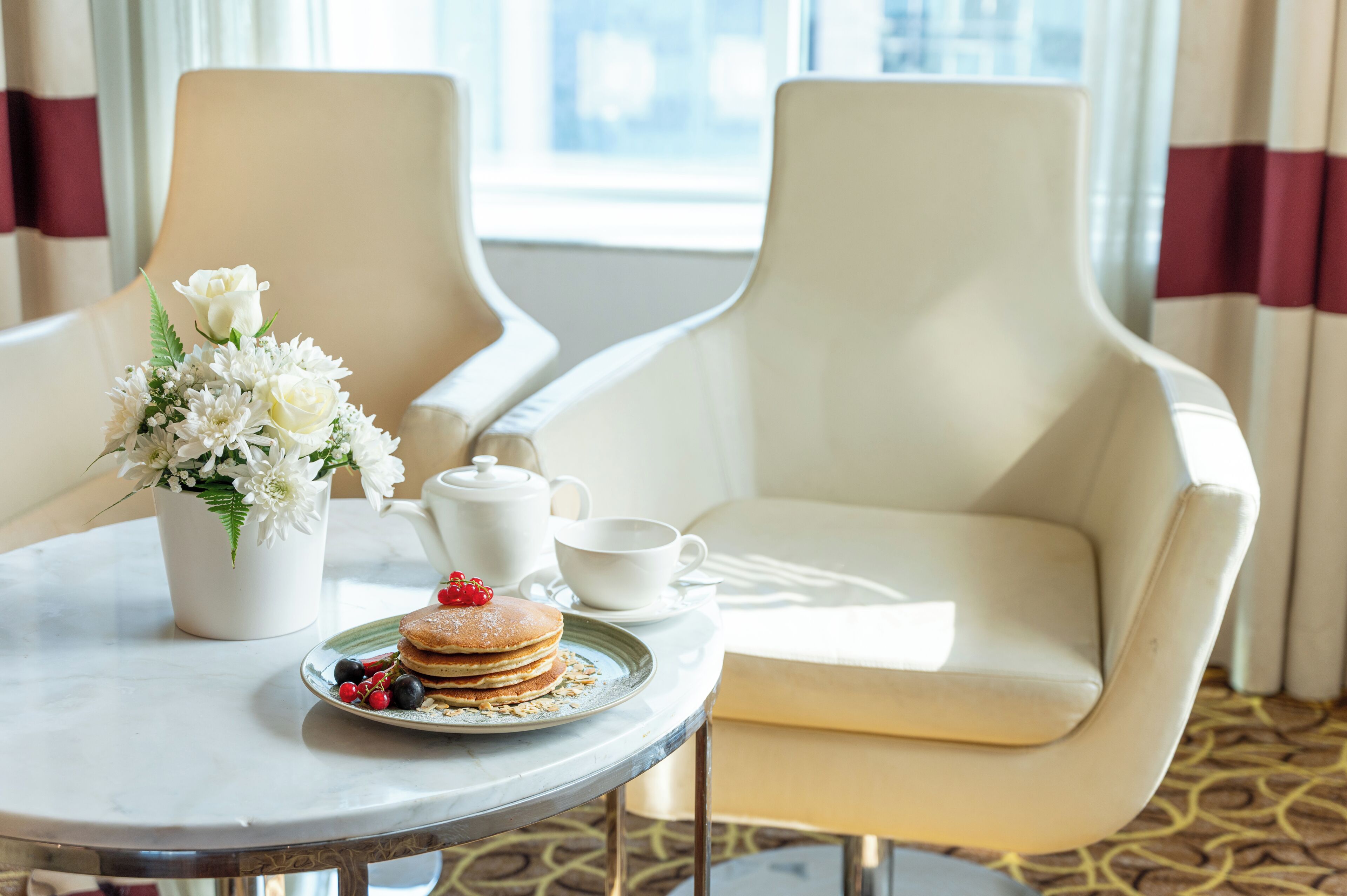A dining table with a floral arrangement, a plate of pancakes, and a teapot.