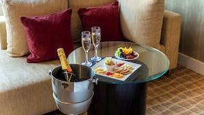 A glass-top table with a bottle of champagne, two glasses, and a plate of fruit and snacks.