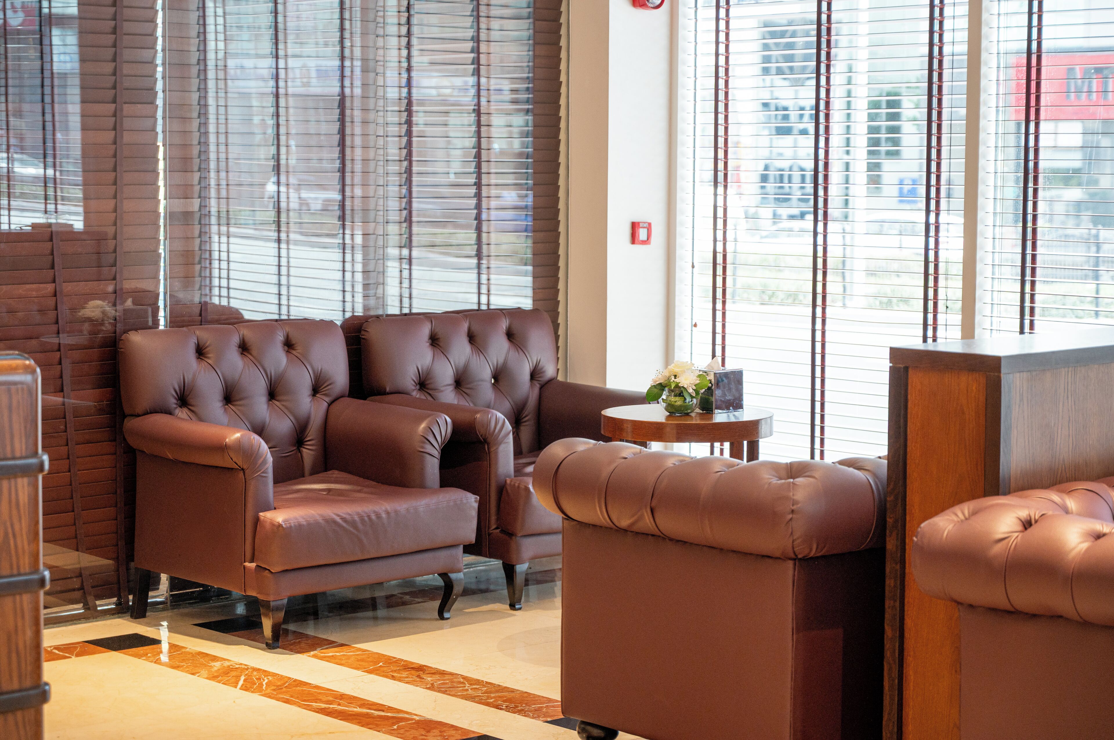 A modern lobby with leather sofas, a small round table, and large windows with blinds.