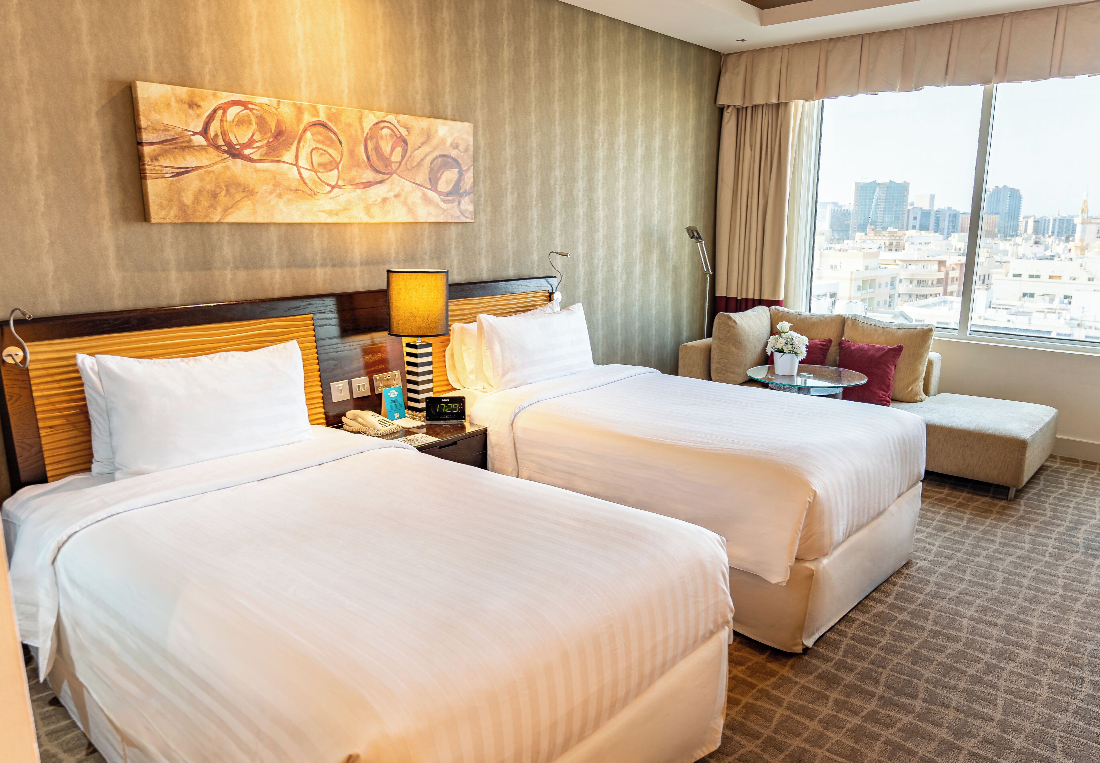 A hotel room with two beds, a sofa, a small table, a lamp, and a painting on the wall.