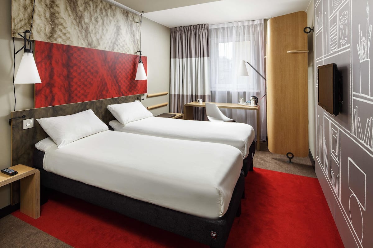 Une chambre d’hôtel avec deux lits, un bureau, une télévision et une moquette rouge.