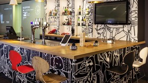 Un espace bar comprenant un comptoir, des tabourets de bar, un téléviseur fixé au mur et un mur décoré de motifs.