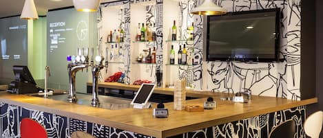 Zona de bar con mostrador, taburetes y una televisión montada en la pared, además de un revestimiento mural con diseño.