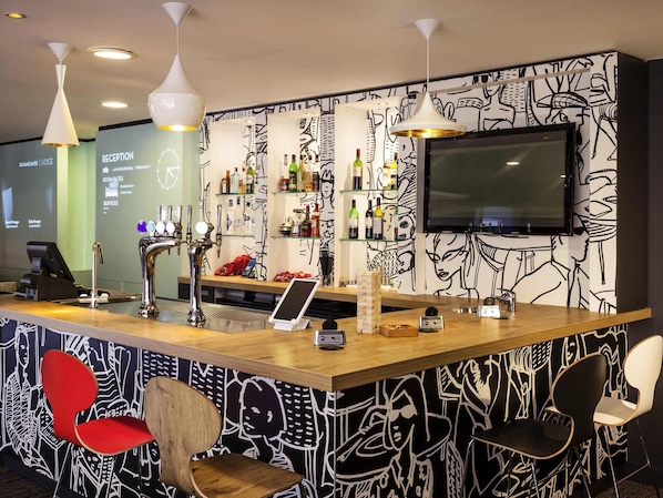 A bar area with a counter, bar stools, a TV mounted on the wall, and a patterned wall.