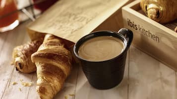 A wooden tray with croissants, a black cup of coffee, and a paper bag with text.