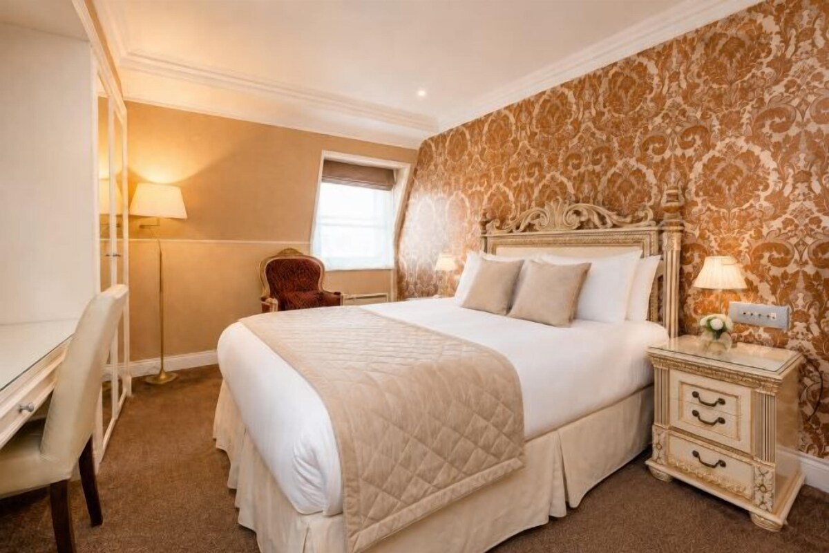 A hotel room with a large bed, bedside tables, a desk, and a chair.