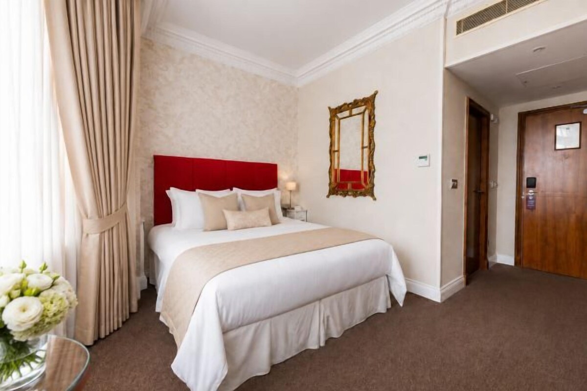 A hotel room with a large bed, a red headboard, a mirror on the wall, and a door to the right.