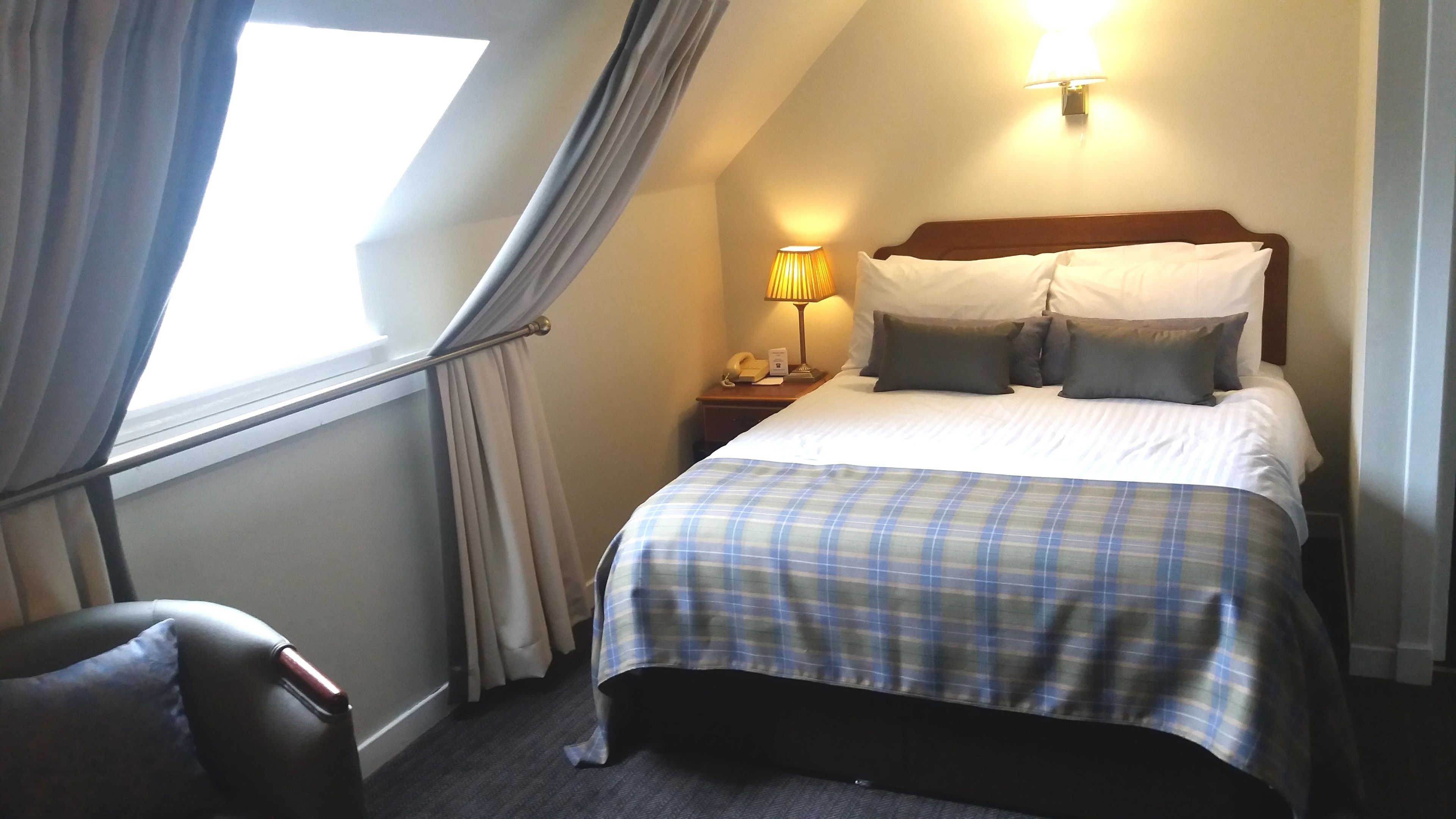 A hotel room with a bed, a nightstand with a lamp, a telephone, and a chair.
