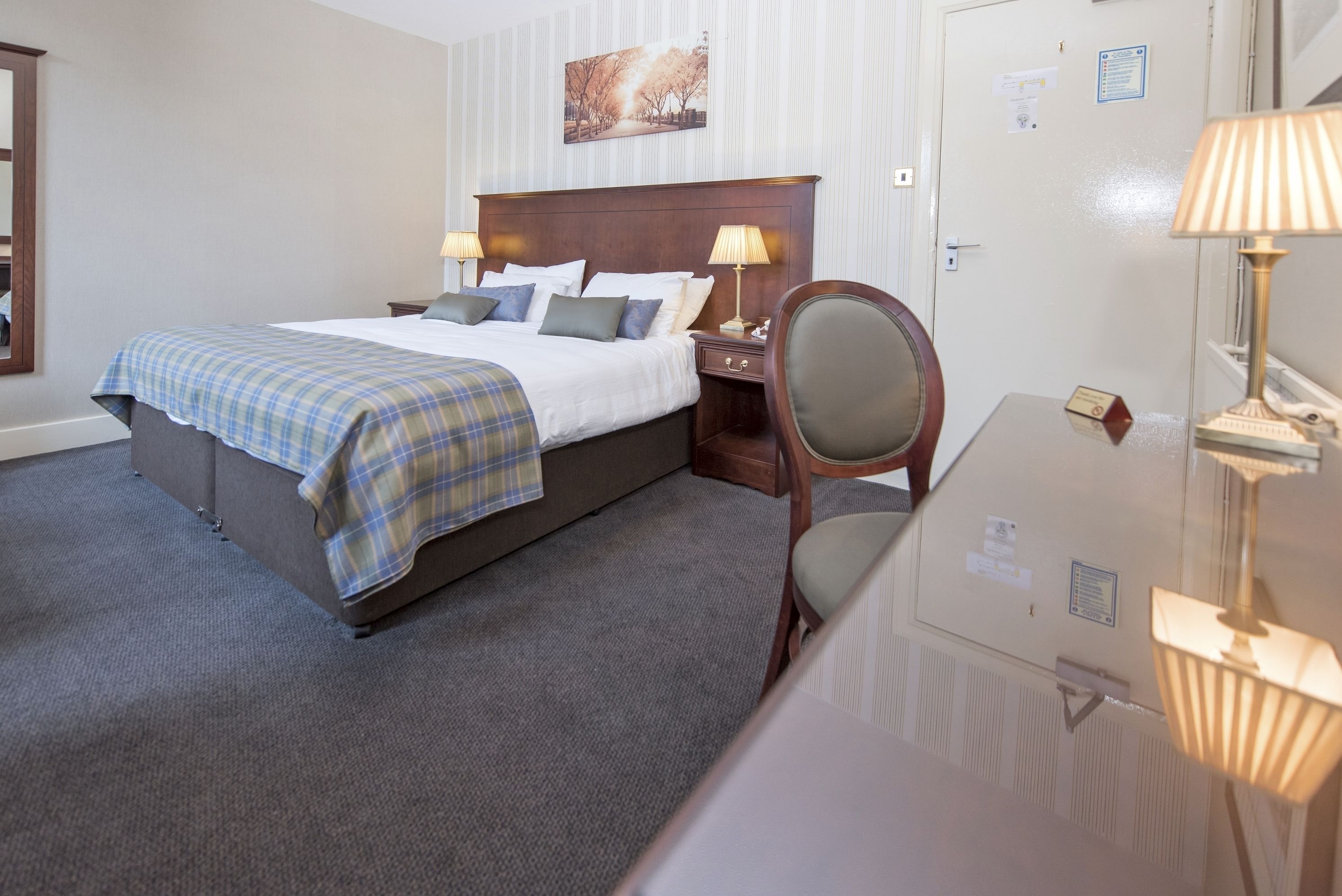 Quarto de hotel com uma cama grande, duas mesas de cabeceira com abajures, uma cadeira e um espelho.