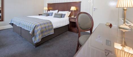 Quarto de hotel com uma cama grande, duas mesas de cabeceira com abajures, uma cadeira e um espelho.