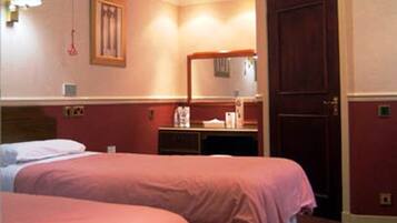 A hotel room with two beds, a desk, a chair, a mirror, and a door.