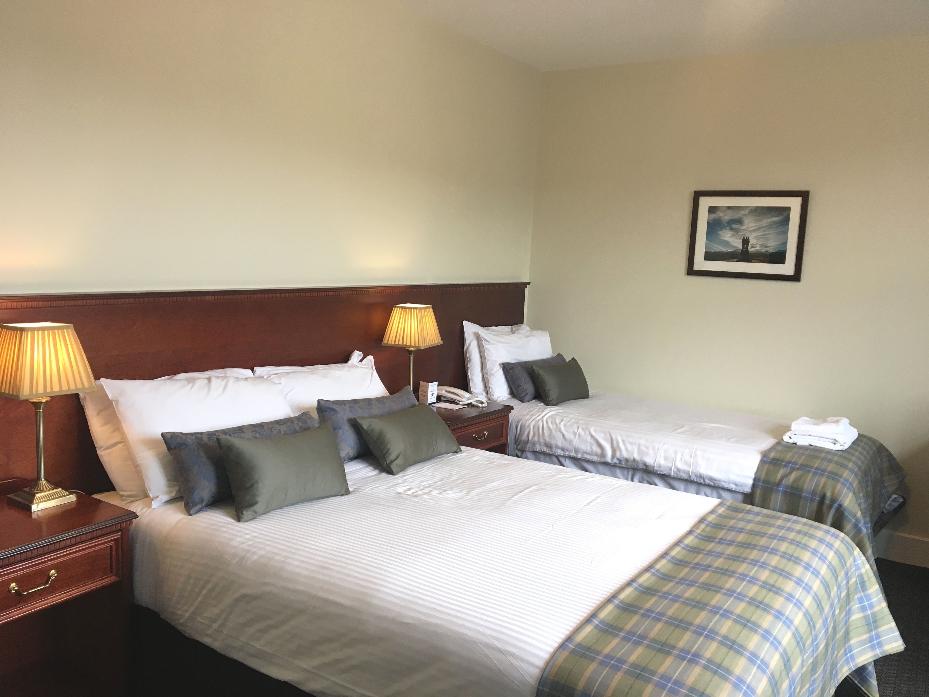 A hotel room with two beds, each with a headboard, bedside tables, lamps, and a framed picture on the wall.