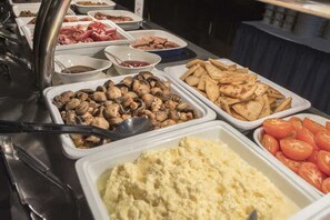A buffet with various food items including mushrooms, potatoes, and tomatoes.
