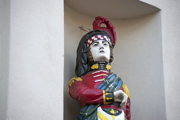 Una estatua de una figura con uniforme rojo y amarillo y un sombrero rojo, ubicada frente a una pared lisa.