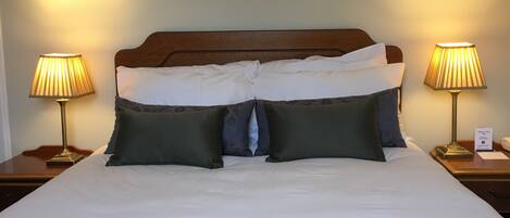 Un letto rifatto con cura, con lenzuola bianche e numerosi cuscini, affiancato da due comodini con lampade.