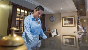 A person in a blue uniform standing in a room with a large glass table, wooden cabinets, and framed pictures on the walls. - Salutation Hotel (Perth)