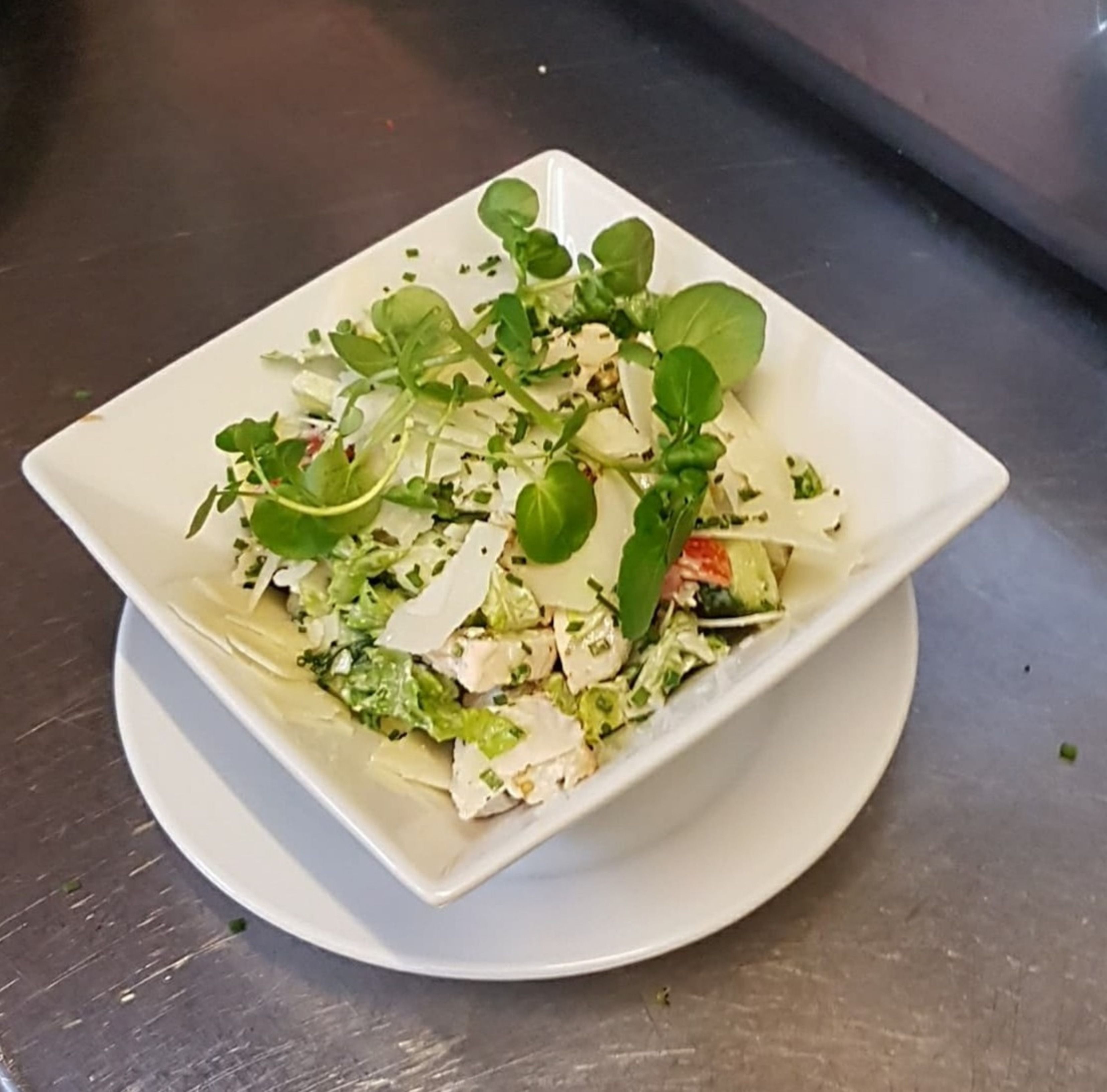 Un piatto bianco quadrato con un'insalata su un piatto bianco rotondo.