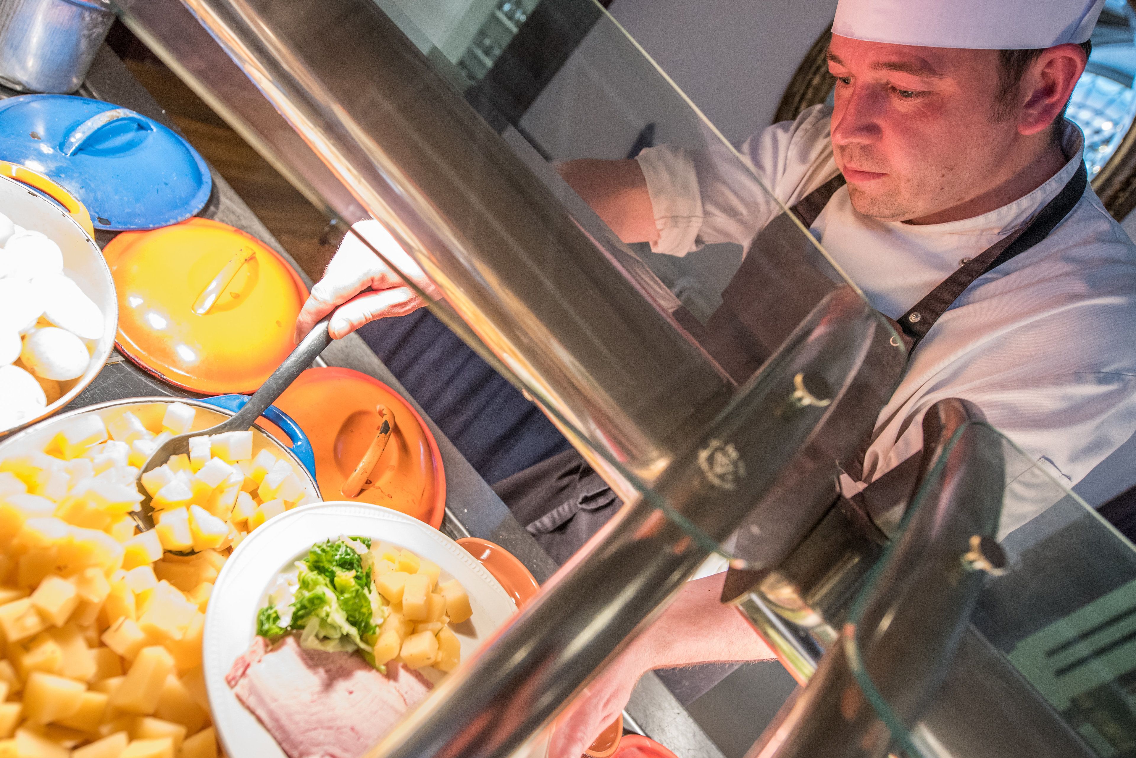 A chef preparing food in a kitchen with various dishes and utensils visible.