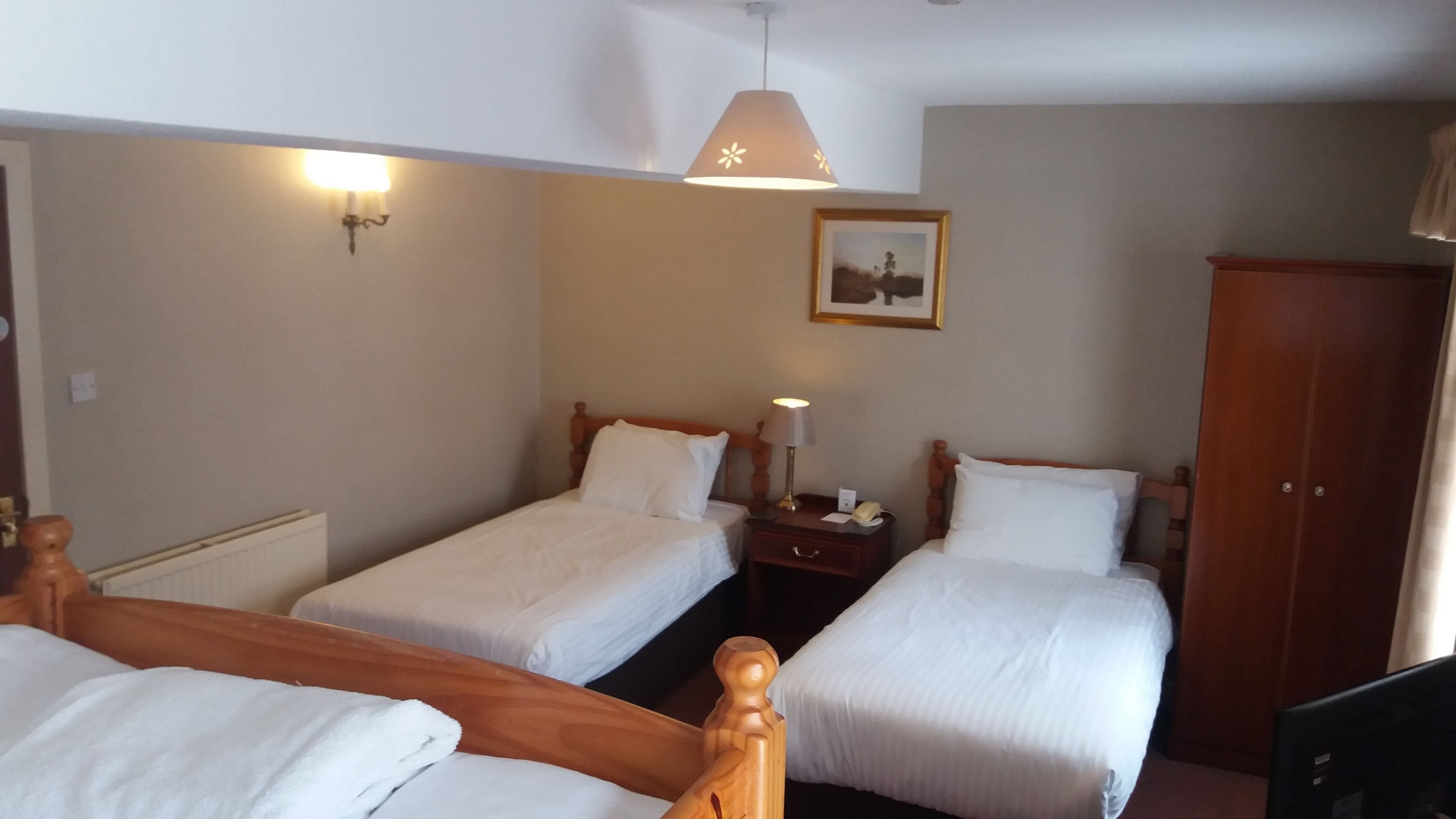 Habitación de hotel con dos camas individuales, un armario de madera, una mesita de noche con lámpara y una lámpara de pared.