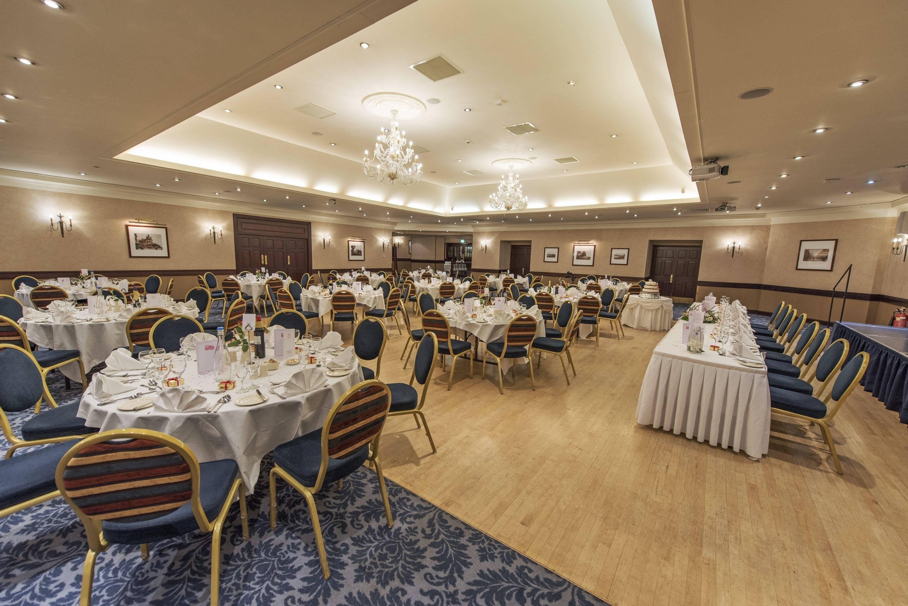 A large banquet hall with round tables set for dining, featuring gold chairs and white tablecloths.